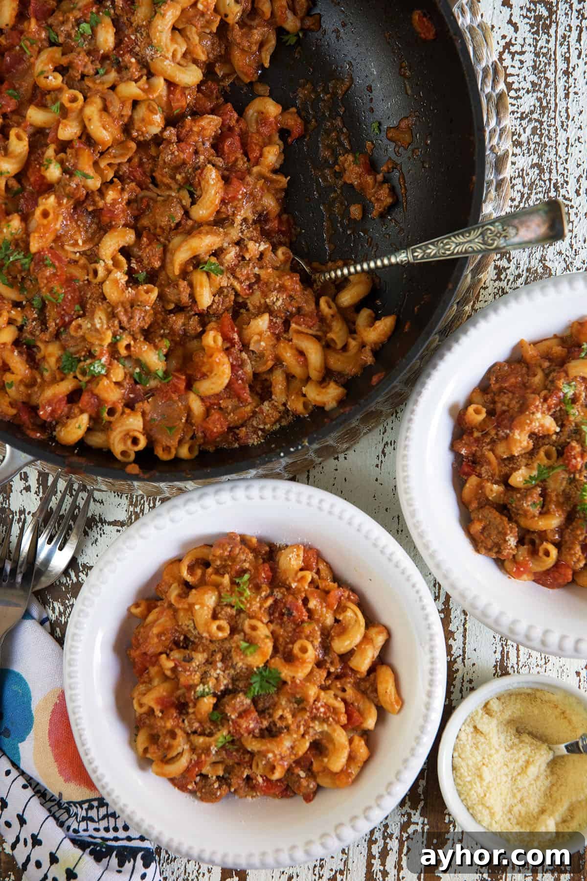Classic American Goulash Recipe: Hearty One-Pot Comfort Meal 5 Goulash is being scooped from a pan and placed into two white bowls.