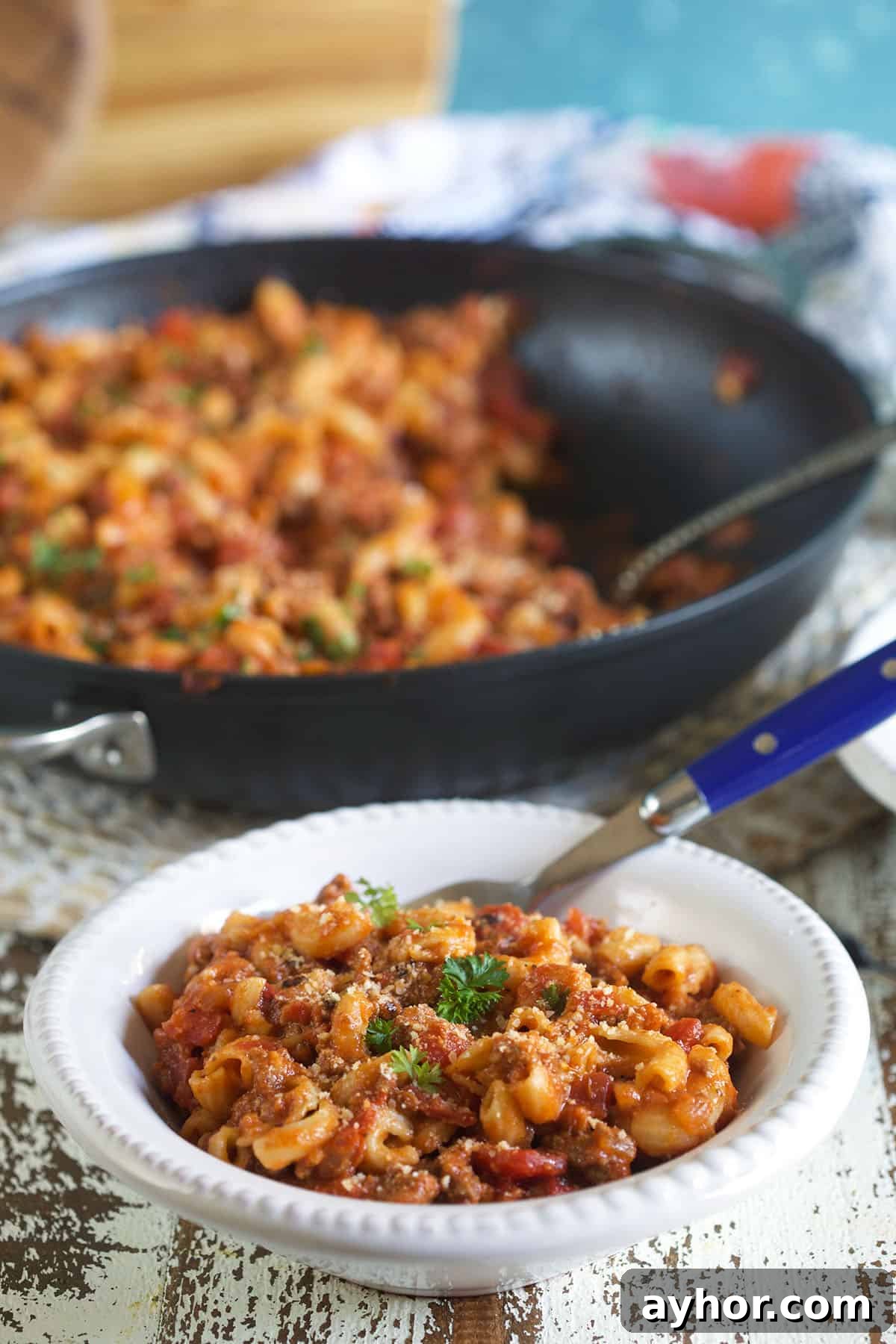 Classic American Goulash Recipe: Hearty One-Pot Comfort Meal 6 A white bowl filled with goulash is set next to a half full pan of more goulash.