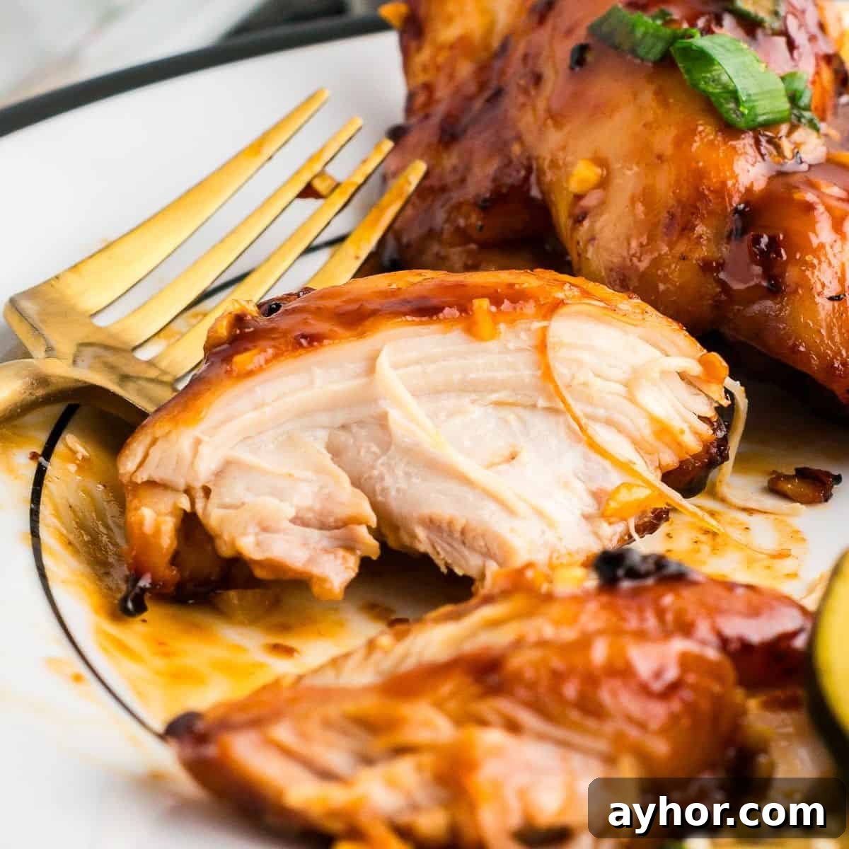 Sticky Air Fryer Chicken Thighs (Oven Method Included) 2 A piece of chicken thigh on a white plate with a gold fork.