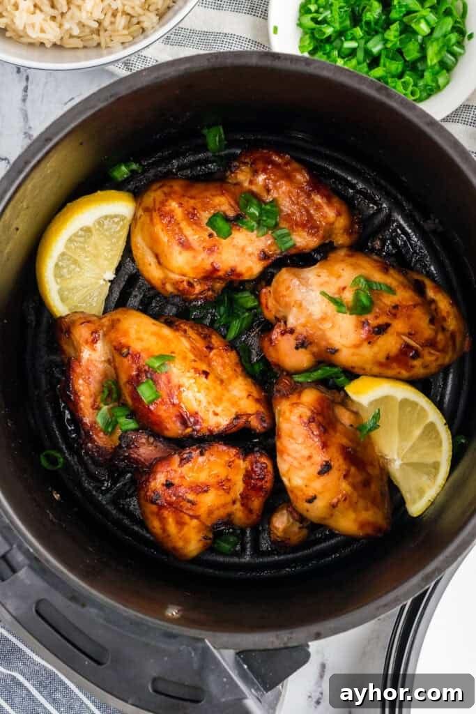Sticky Air Fryer Chicken Thighs (Oven Method Included) 7 Boneless marinated chicken thighs in an air fryer basket, garnished with lemon and parsley.