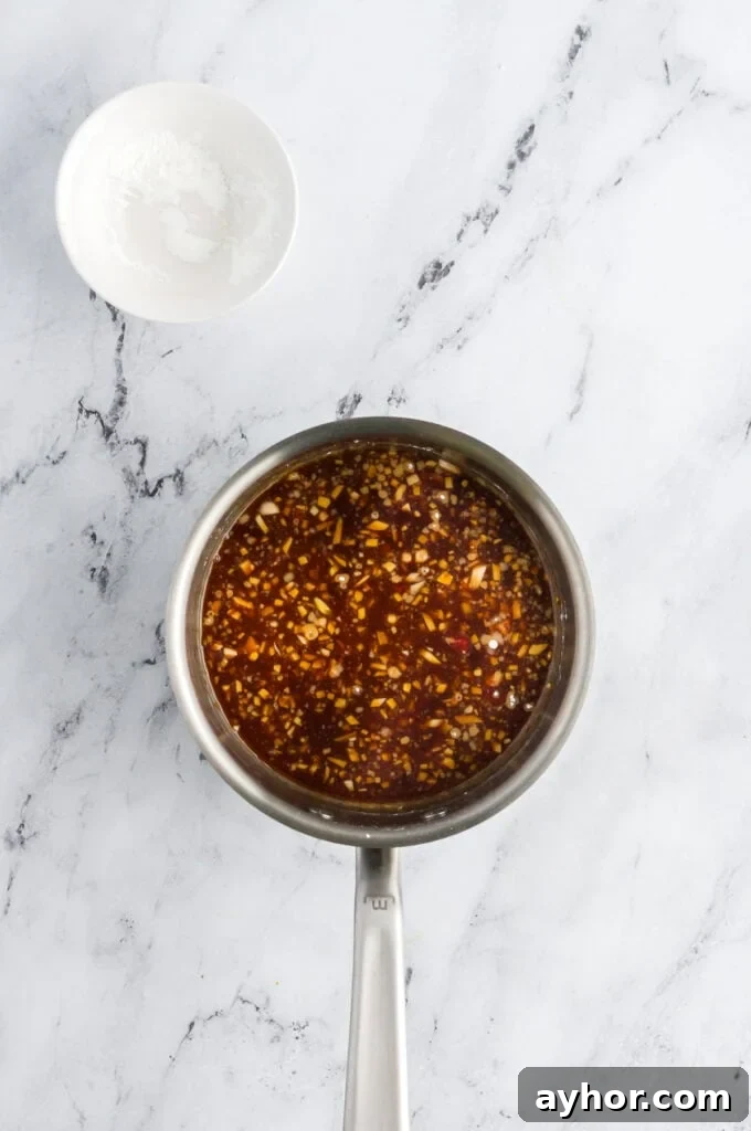 Sticky Air Fryer Chicken Thighs (Oven Method Included) 8 Sauce pan with sticky sauce for air fryer chicken thighs sitting next to a bowl of cornstarch.
