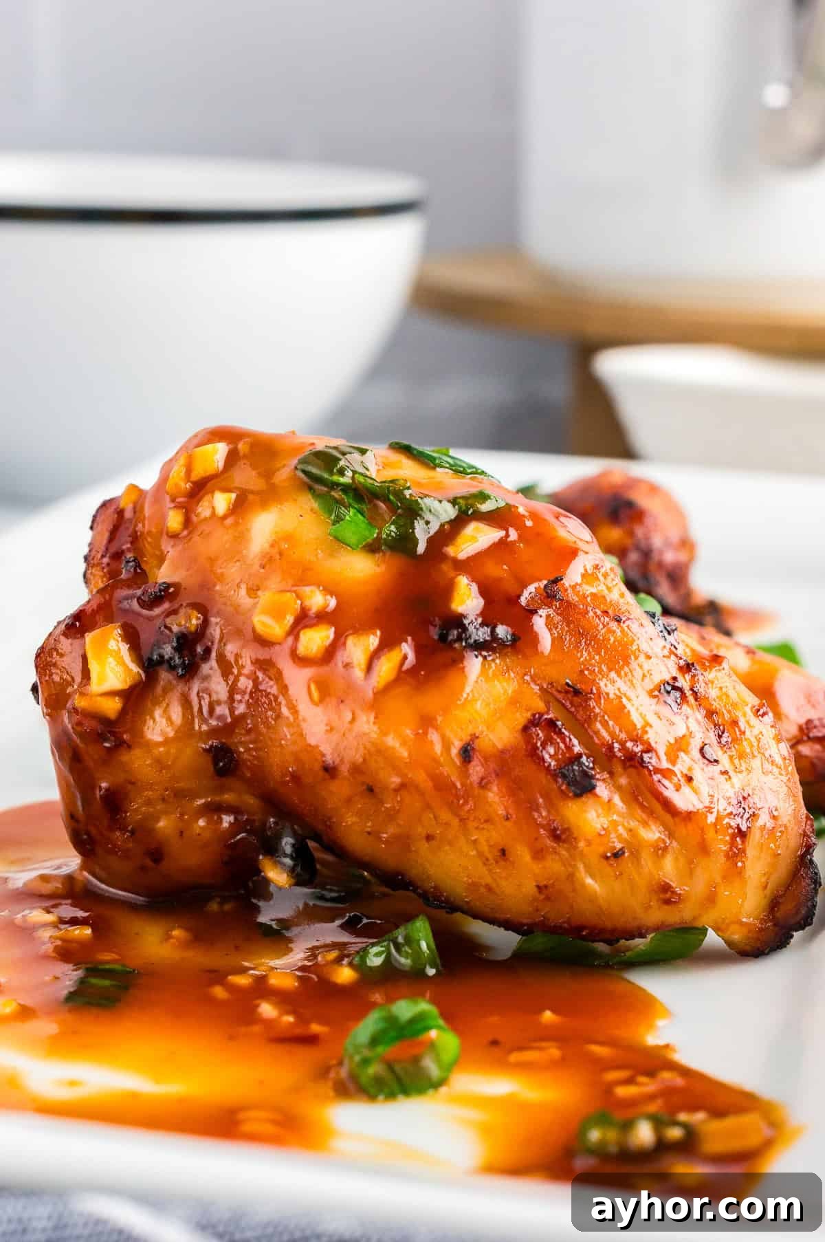 Sticky Air Fryer Chicken Thighs (Oven Method Included) 10 Close up shot of sticky air fryer chicken thighs on a white plate shot from the side.