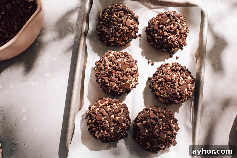 giant chocolate chip covered cookie dough balls on a parchment lined cookie sheet