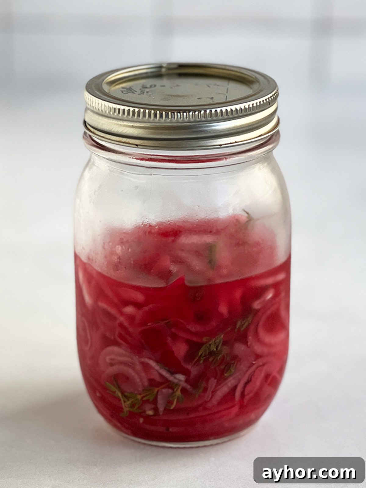 Pickled red onions ready to eat in a larger jar that looks about ⅔ full.