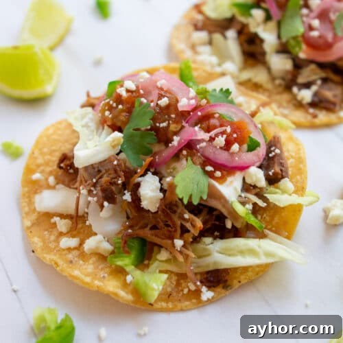 Instant pot carnitas tacos on a white background with limes on the side.