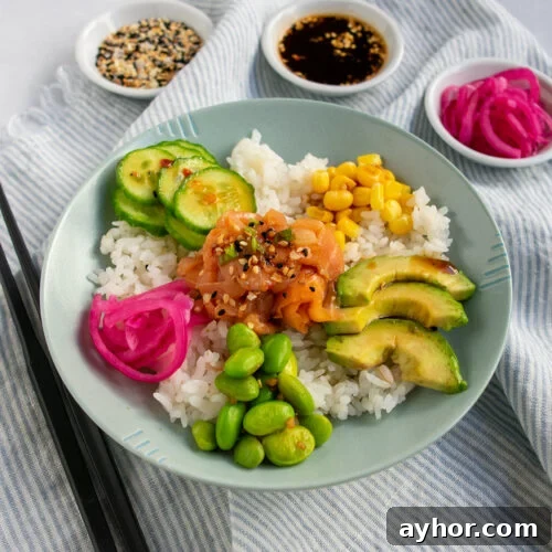 Smoked salmon poke bowl at an angle on a striped light blue napkin with black chopstics and 3 white bowls of seasonings in the back.