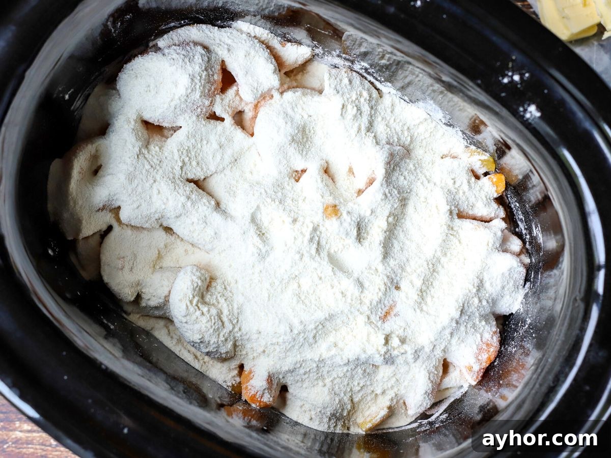 Slow-Cooker Peach Cobbler Recipe: Juicy Homemade Dessert 5 peaches in a crock pot with flour and sugar on top.