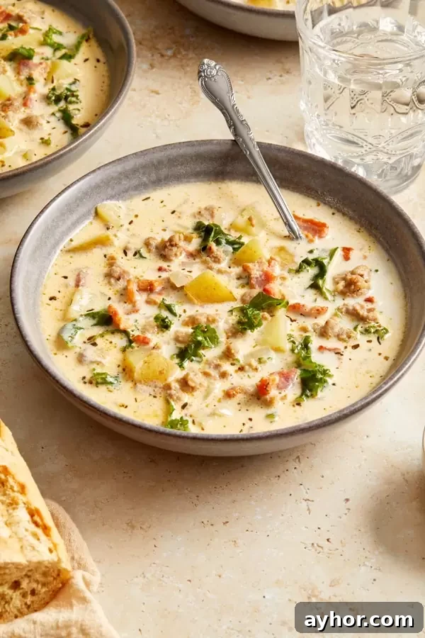 A bowl of Dairy Free Zuppa Toscana Soup with bread and water to the side.