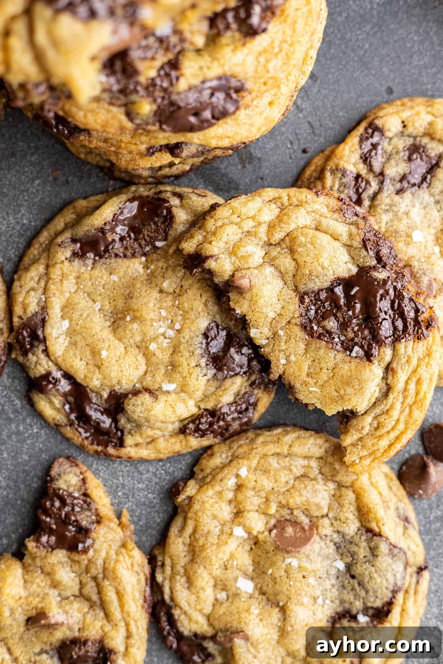 Overhead view of chocolate chip cookies. One broken in half sitting on top of the cookies.