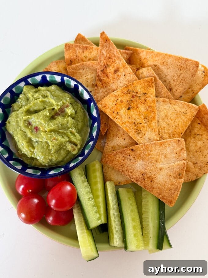 Airfryer Tortilla Chips served on a plate, served with a small bowl of guacamole with chopped cucumber and cherry tomatoes.