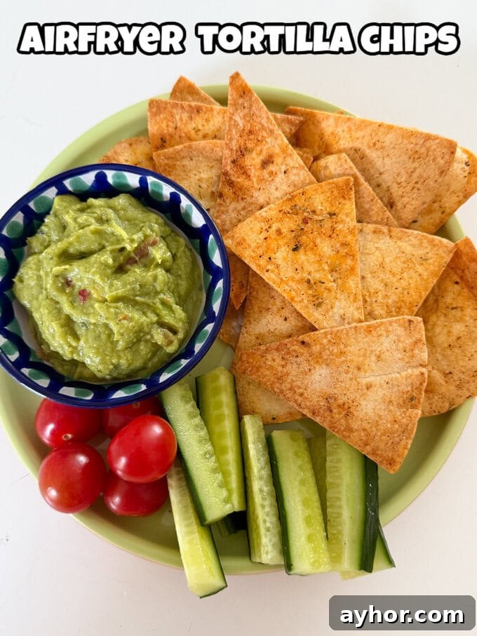 Airfryer Tortilla Chips served on a plate, served with a small bowl of guacamole with chopped cucumber and cherry tomatoes.