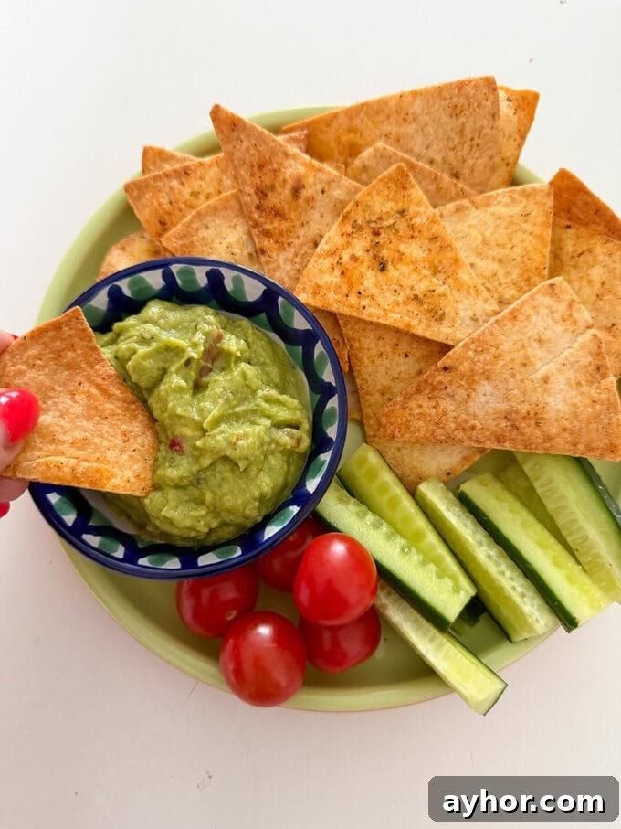 Airfryer Tortilla Chips served on a plate, served with a small bowl of guacamole with chopped cucumber and cherry tomatoes.