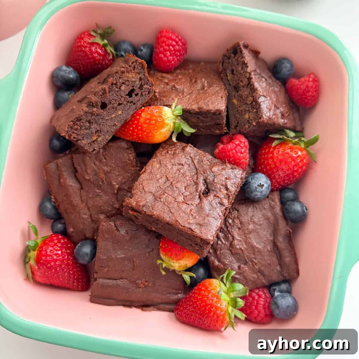 Sweet potato brownies cut into squares, served in a oven proof dish and garnished with whole strawberries and blueberries.