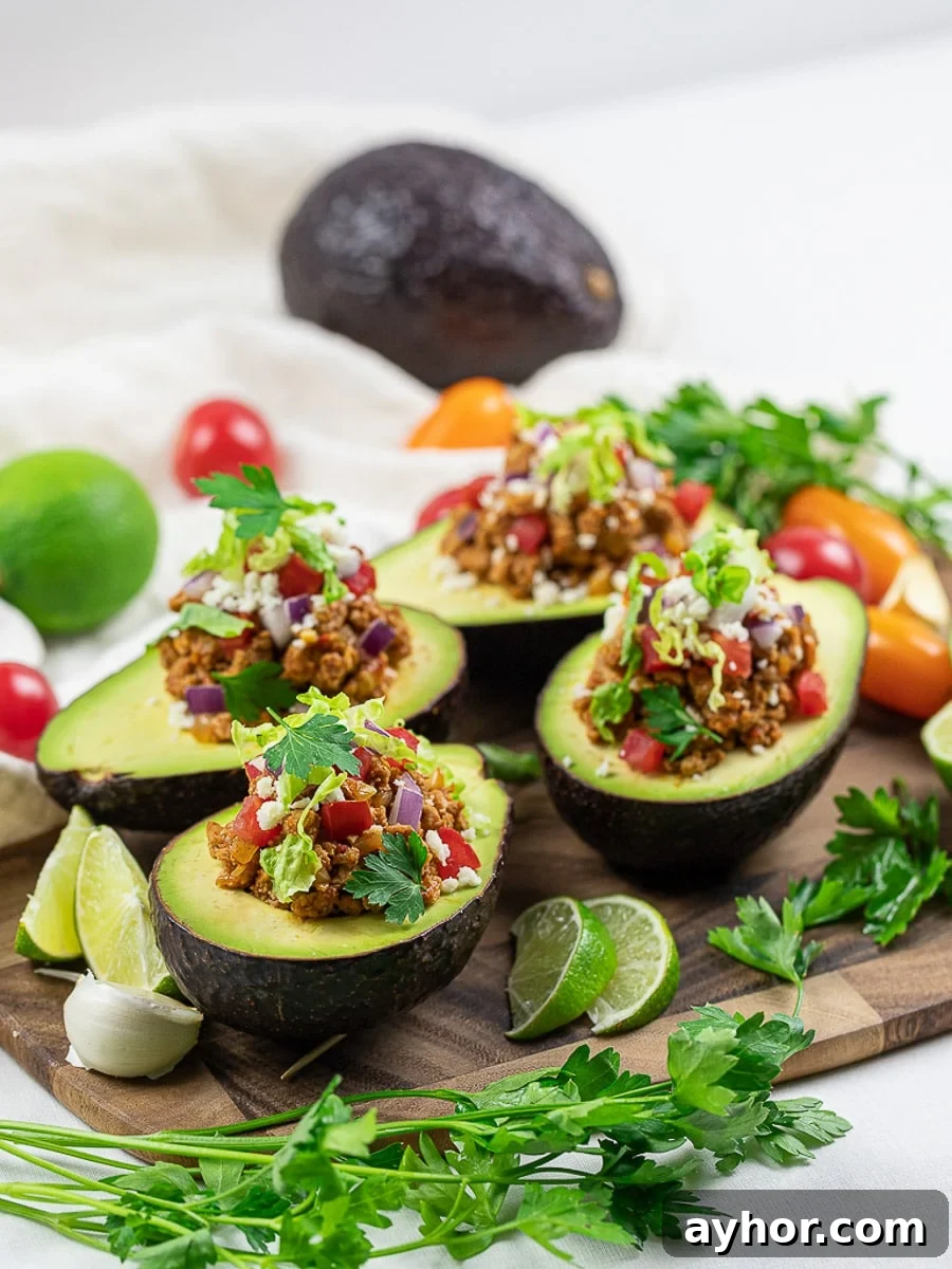 Avocado boats with lime, taco meat, tomatoes, and cilantro on a wooden board.