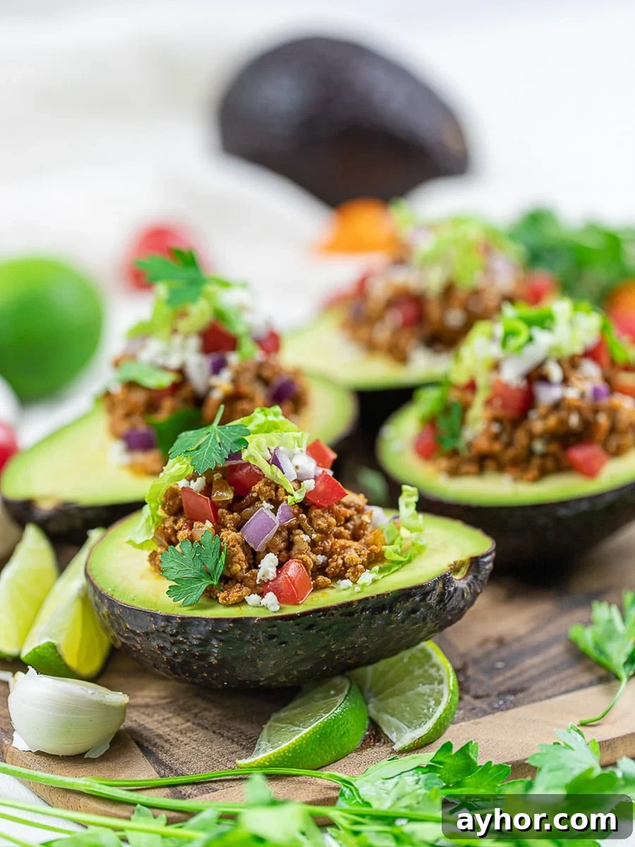 Keto taco avocado boats on a wooden cutting board with lime, taco meat, tomatoes, and cilantro.