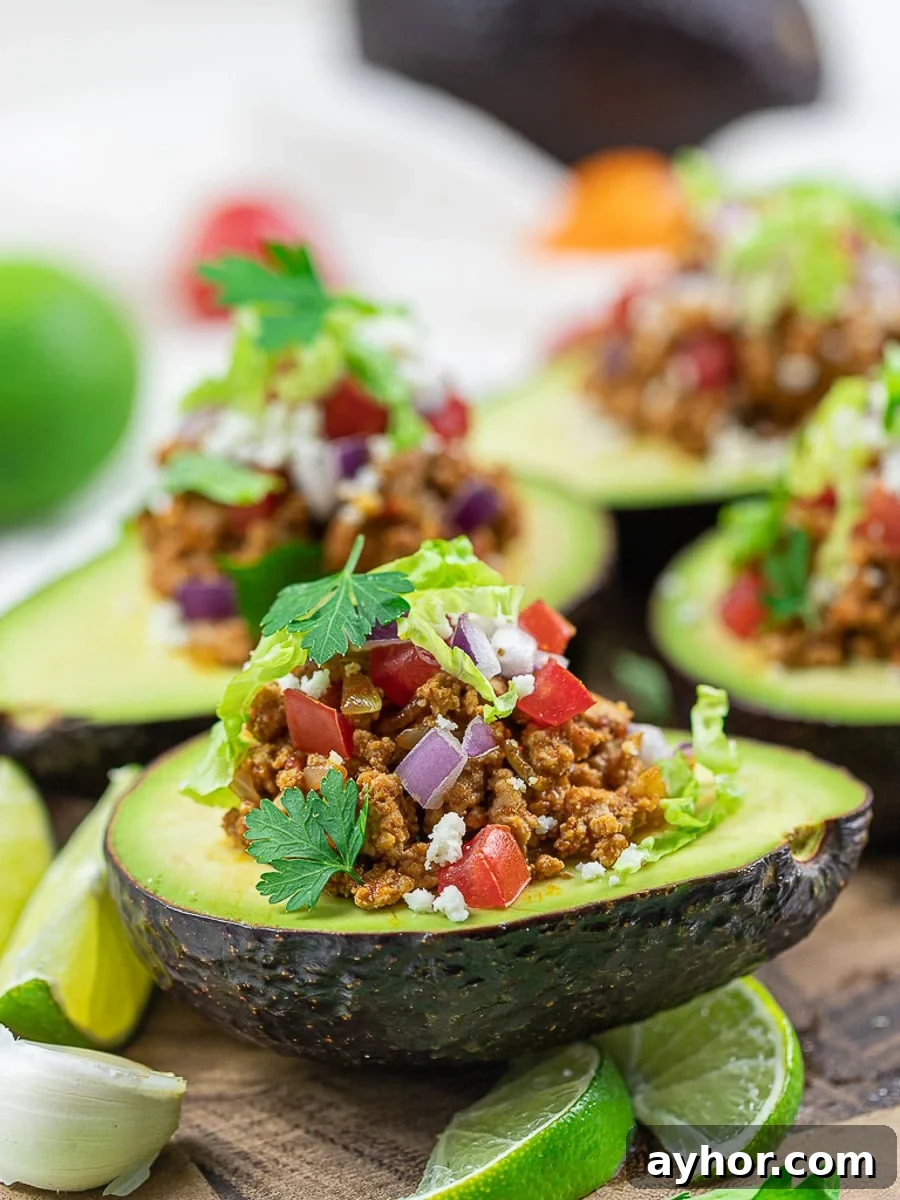 Keto taco avocado boats with lime, taco meat, tomatoes, and cilantro on a white plate.