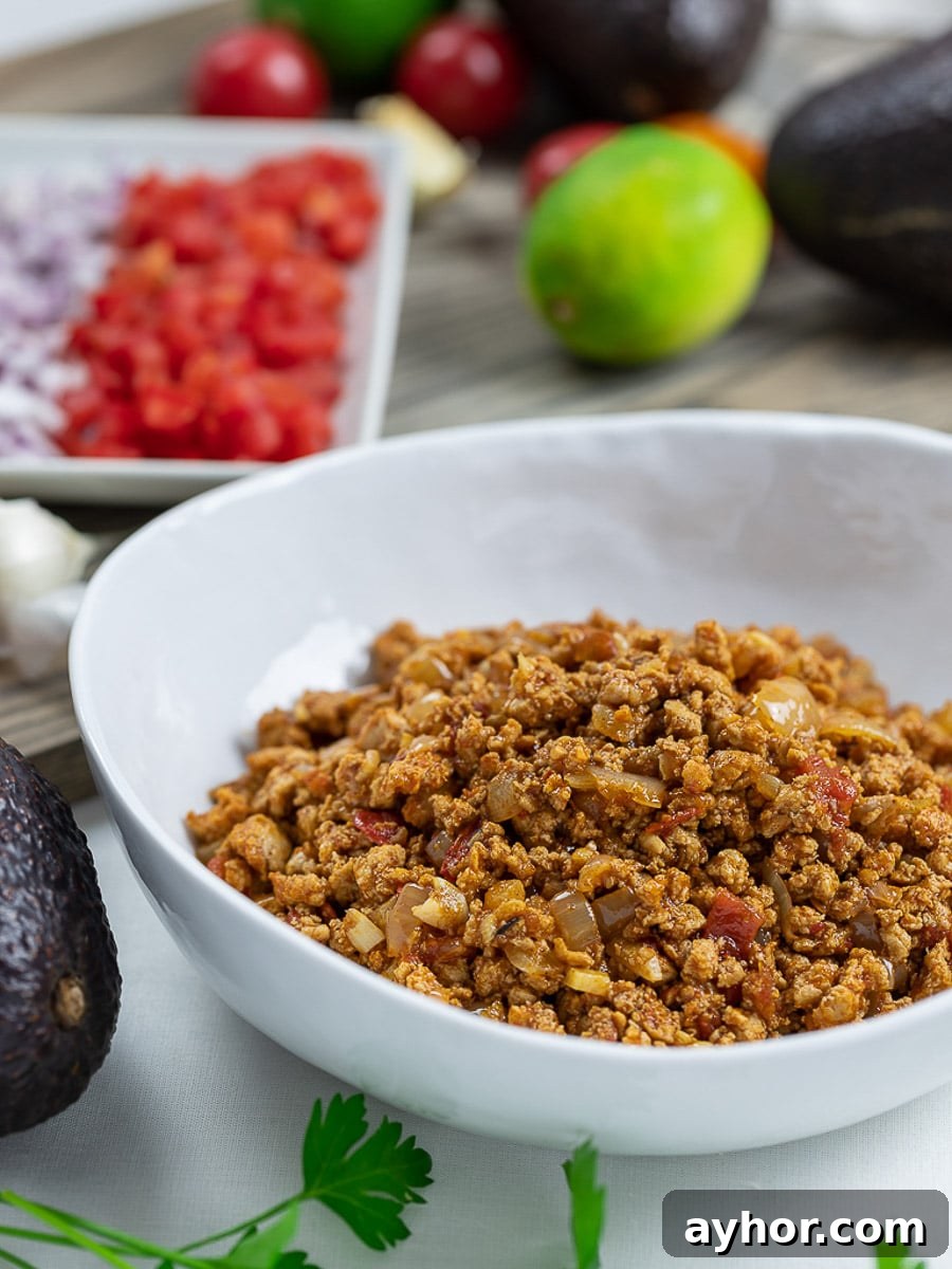 Taco meat filling in a white bowl with tomatoes, lime, and avocado.