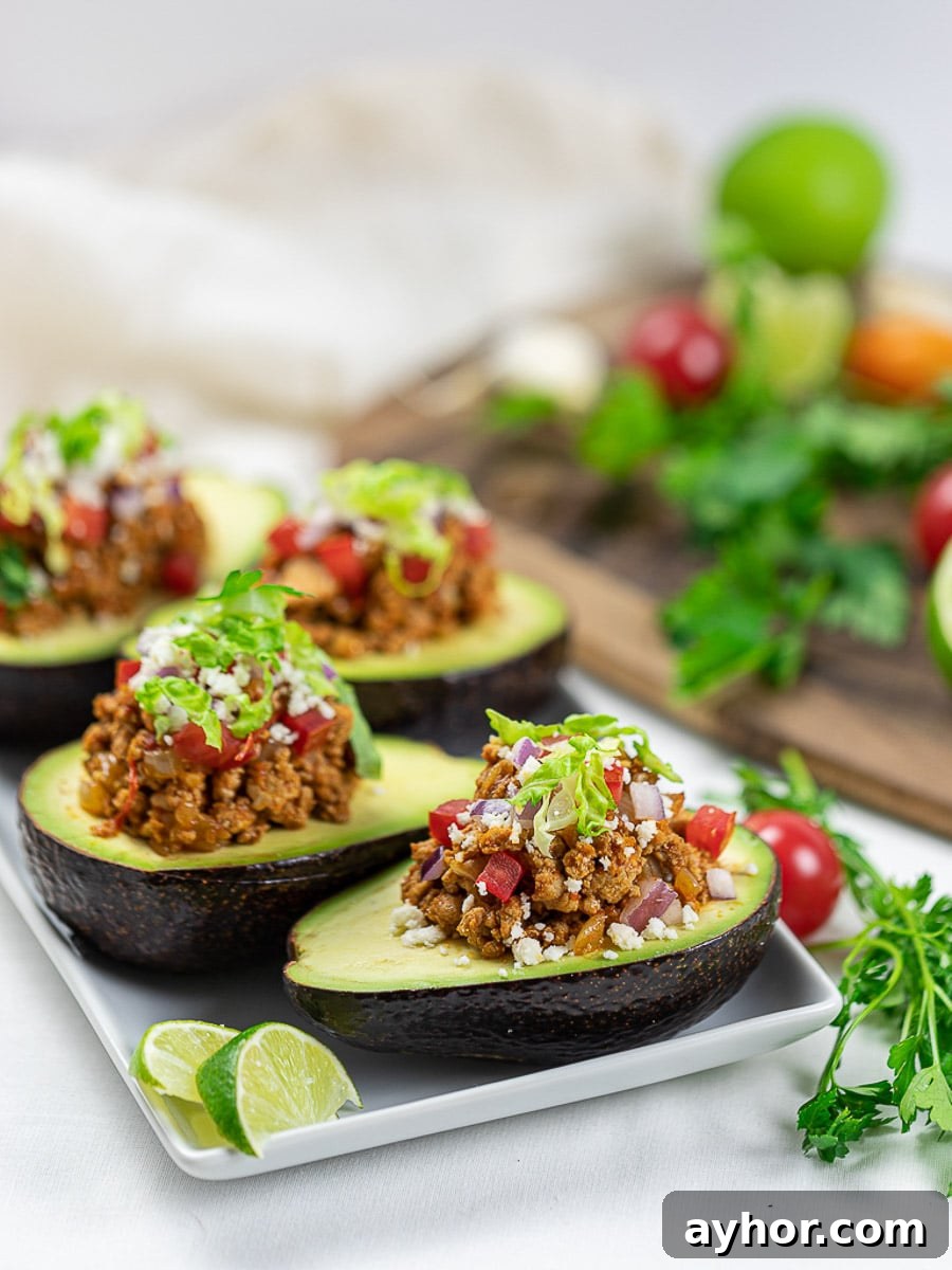Taco stuffed avocado boats with lime, taco meat, tomatoes, and cilantro on a white plate.