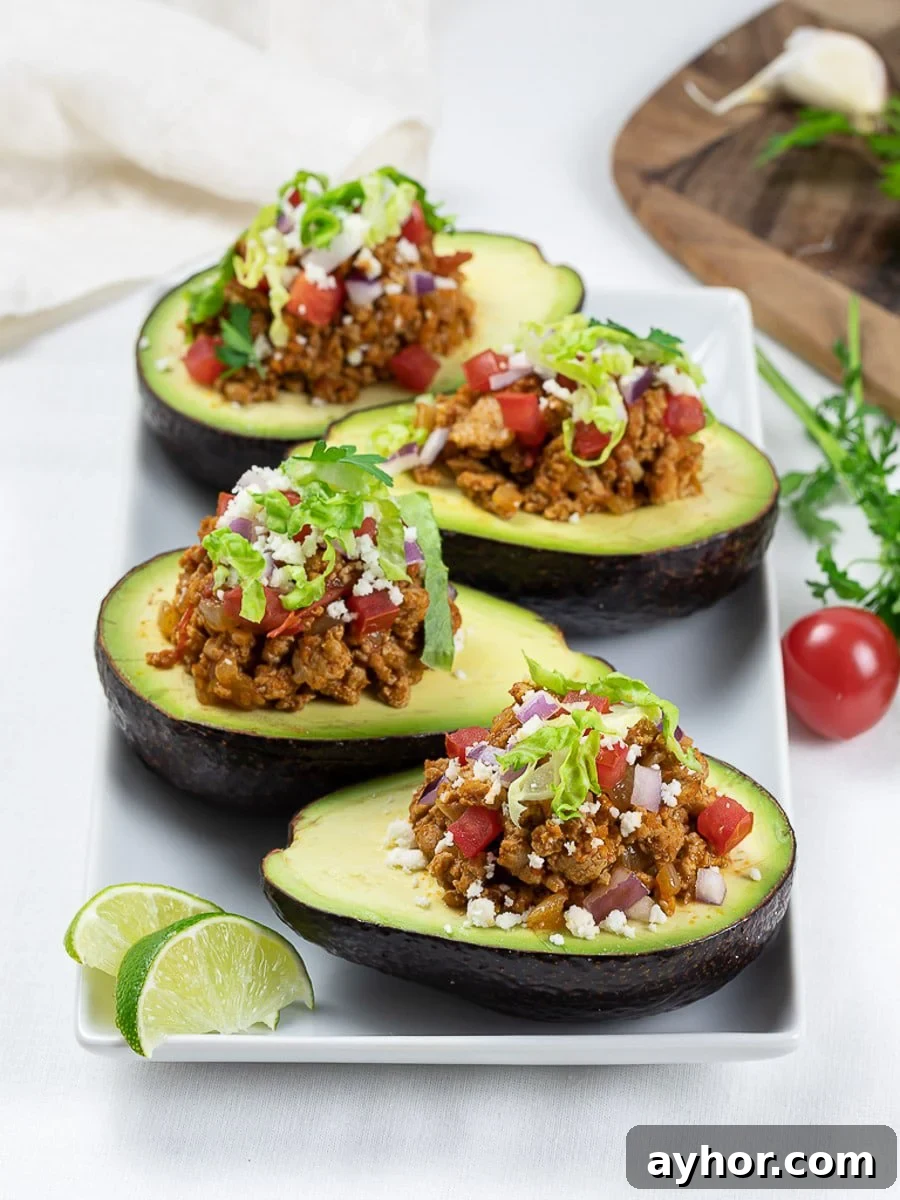 On a white plate, Keto taco stuffed avocado boats with lime, taco meat, tomatoes, and cilantro.