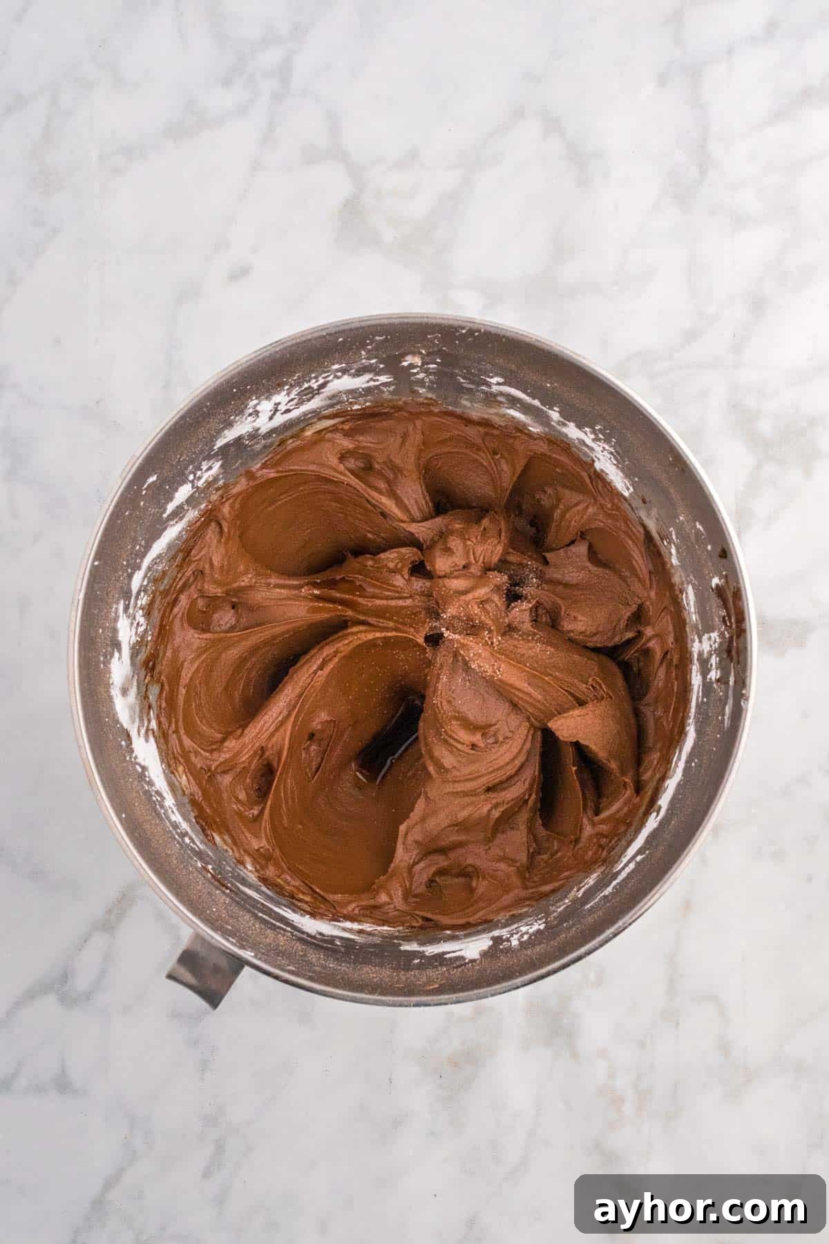 Silky Chocolate Buttercream Frosting Recipe for Cakes and Cupcakes 8 A mixing bowl containing smooth chocolate buttercream icing on a marble countertop.