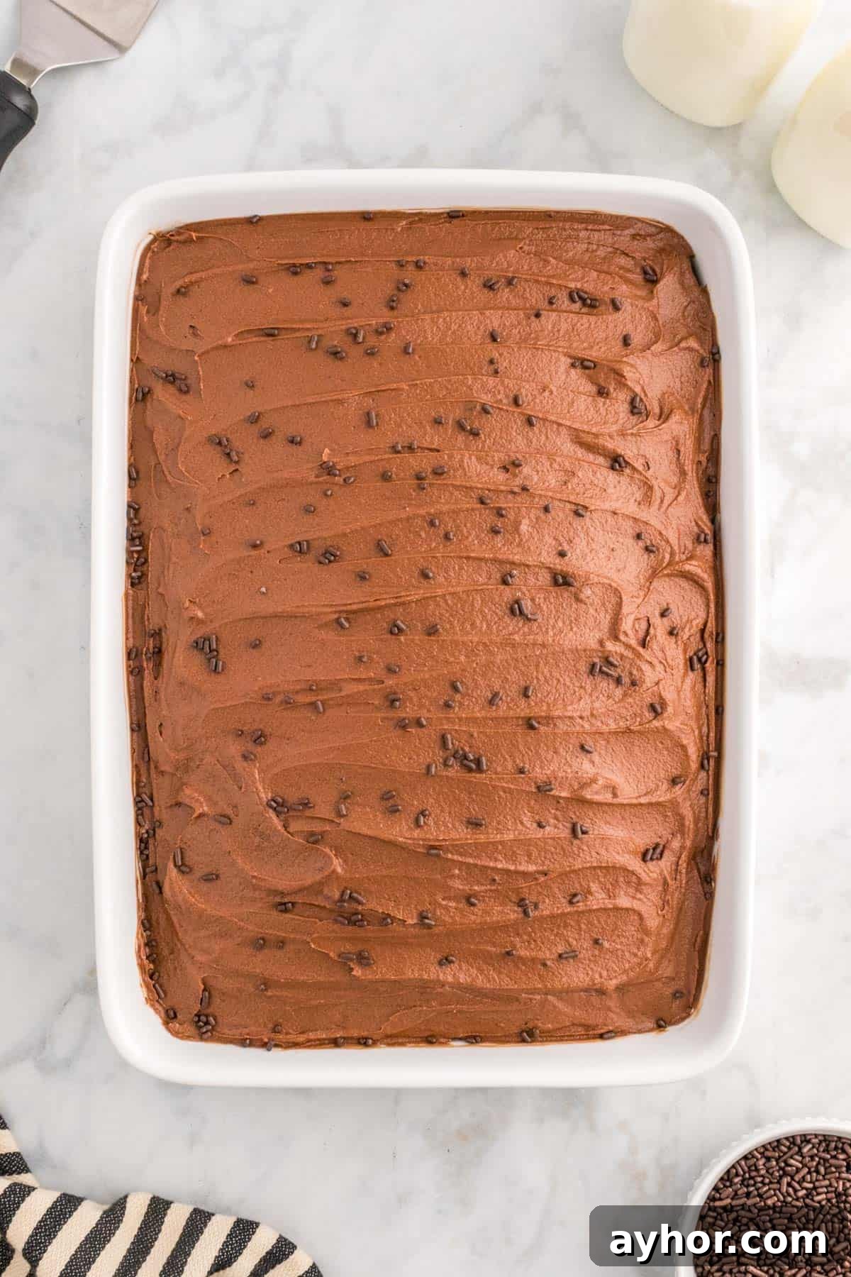 Silky Chocolate Buttercream Frosting Recipe for Cakes and Cupcakes 10 A rectangular cake with chocolate buttercream and sprinkles in a white baking dish on a marble counter.