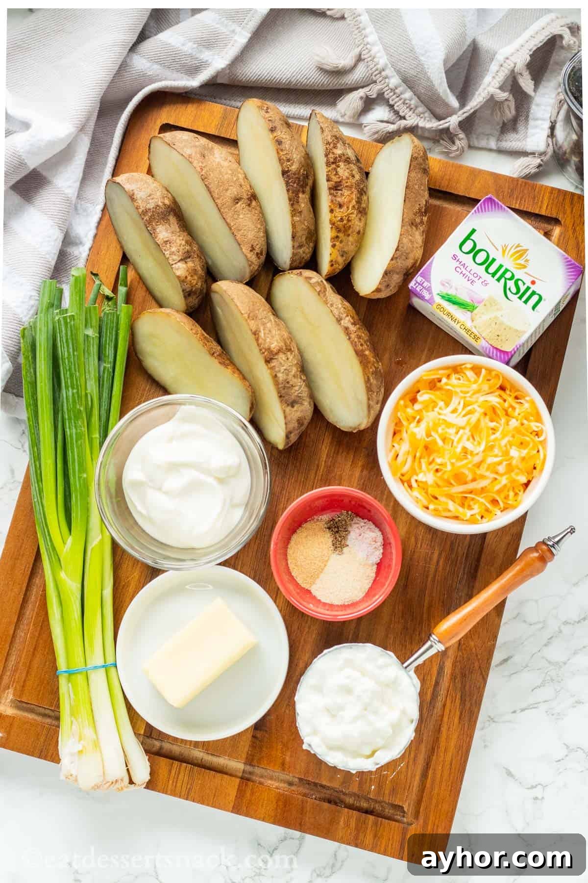 Green onions, sour cream, cottage cheese, cheddar and boursin cheese, potatoes and spices on cutting board.