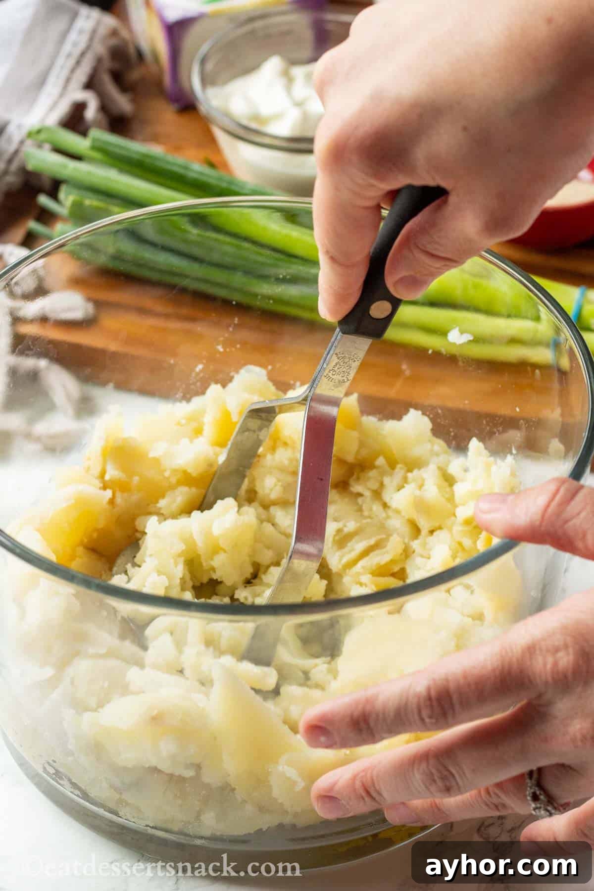 Mashing baked potatoes with potato masher in glass bowl.
