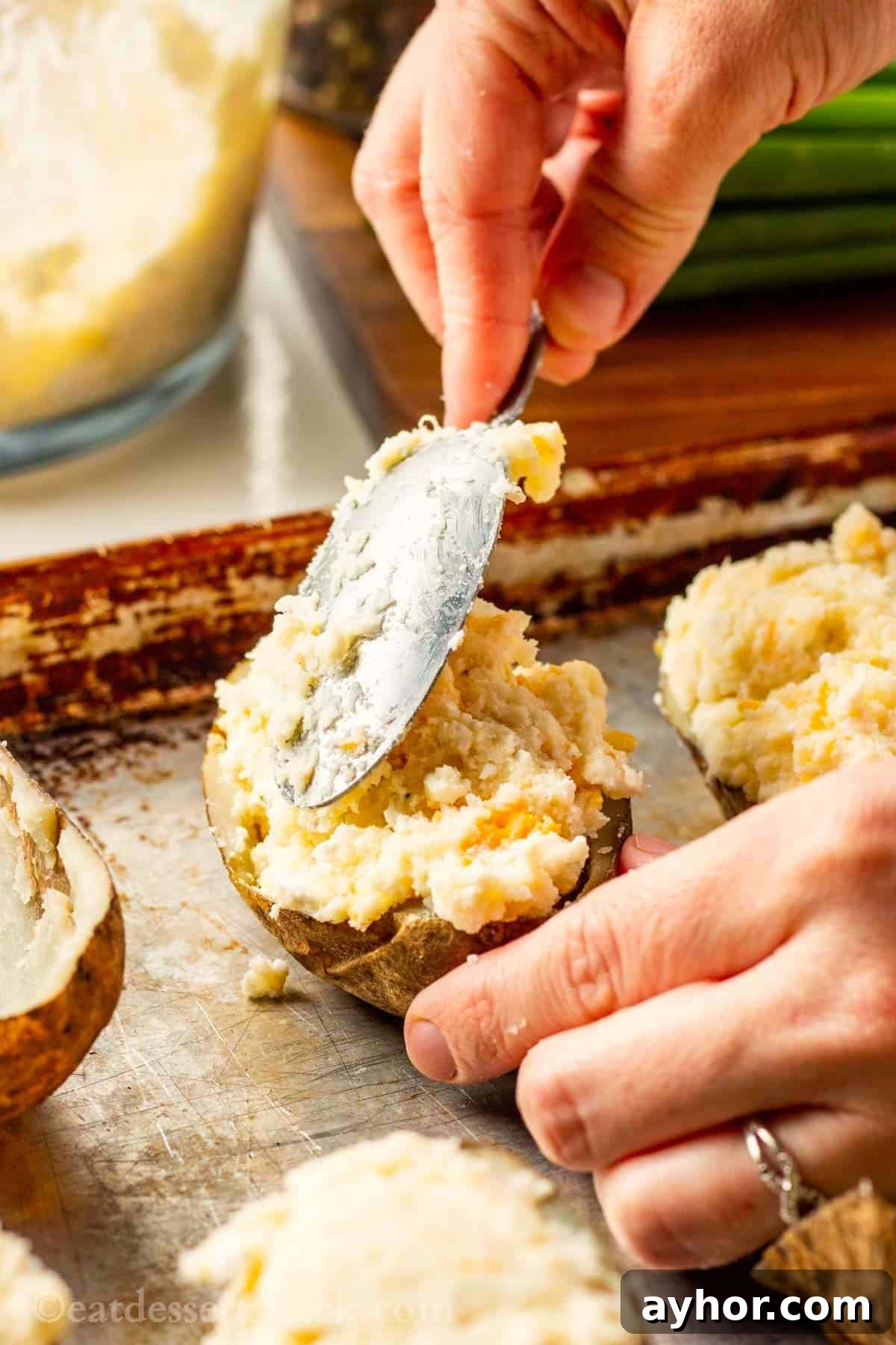 Spoon scooping boursin potato filling into potato skin on metal pan.
