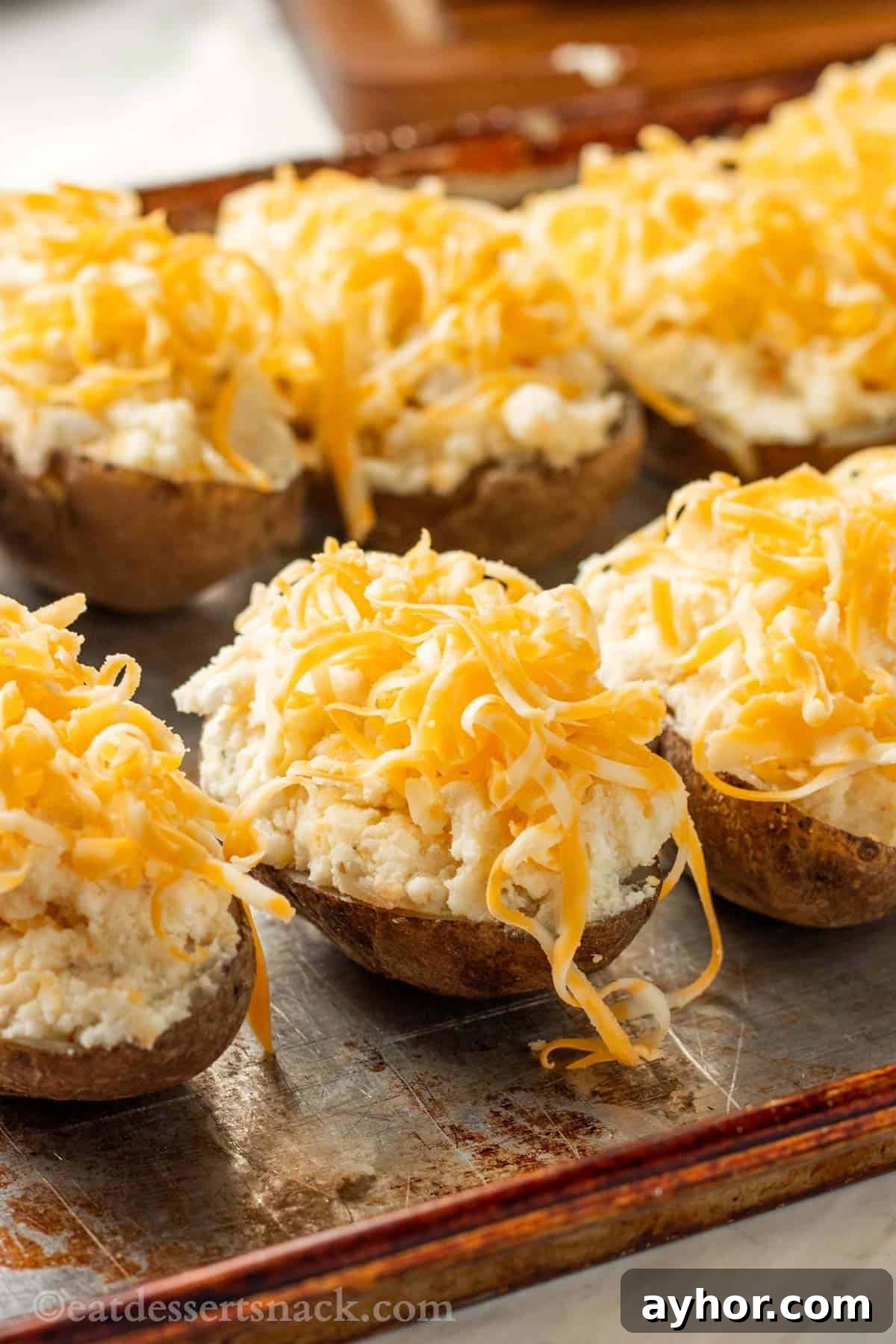 Filled potato skins on metal pan with grated cheddar cheese on top.