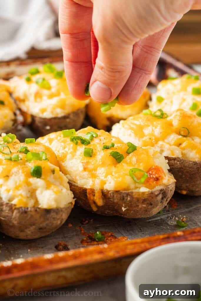 Hand sprinkling green onions on baked boursin stuffed potatoes on metal pan.