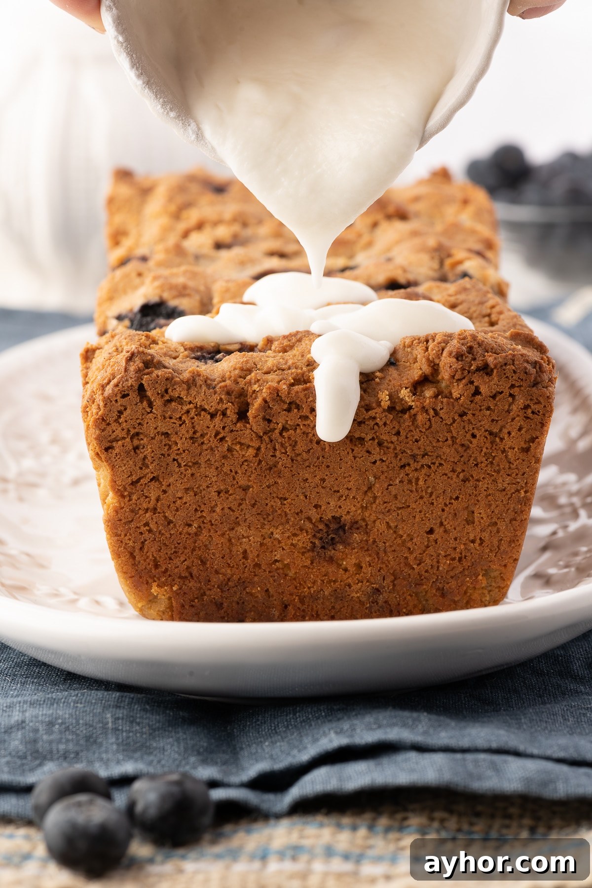 Low-Carb Keto Blueberry Bread with Zesty Lemon Drizzle 4 Pouring icing over a loaf of keto blueberry bread.