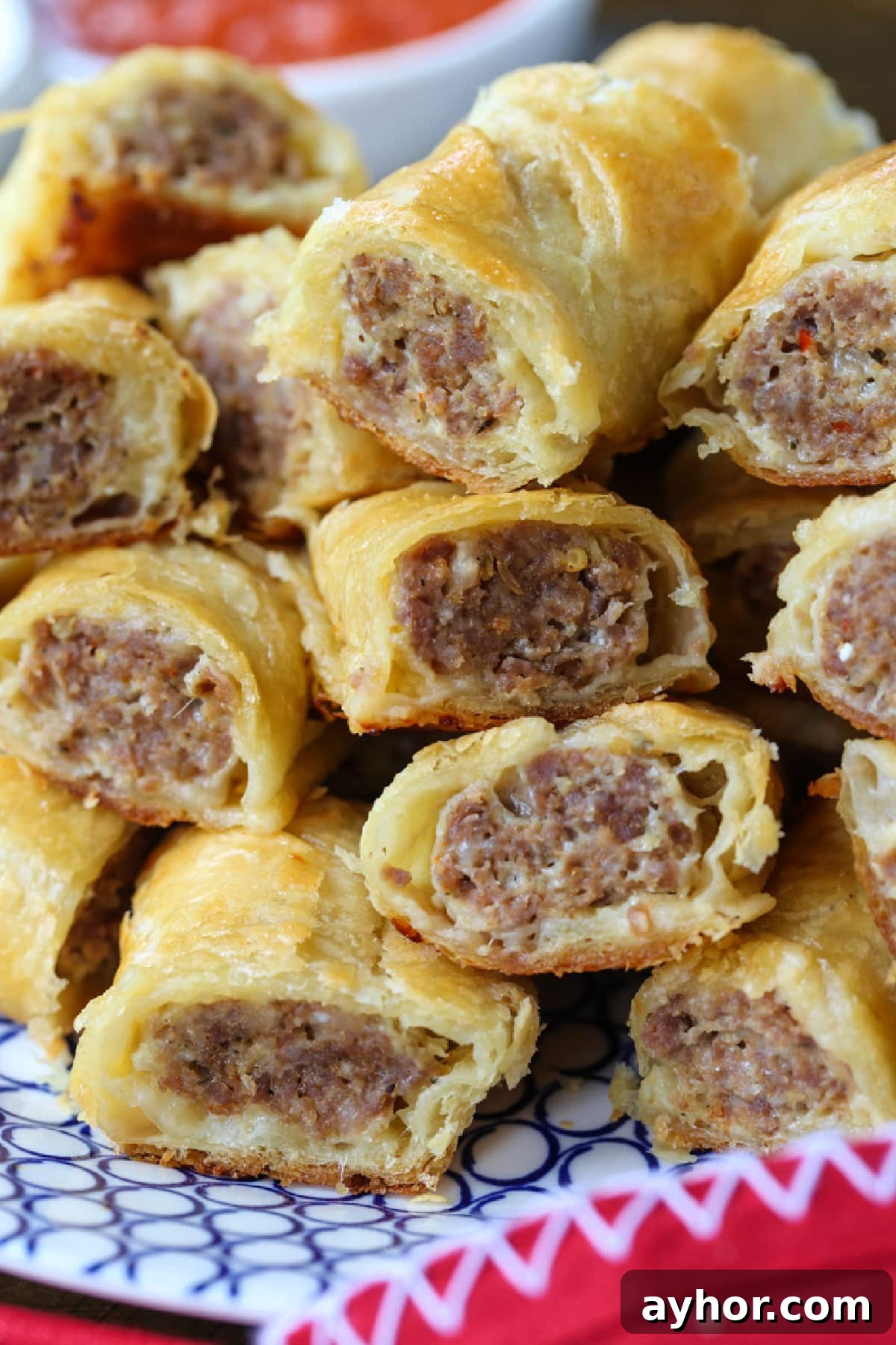 Everyone loves Puff Pastry Sausage Rolls! A buttery, flaky crust with a cheesy sausage filling. Perfect for holidays, parties and game days! sliced sausage rolls stacked on plate