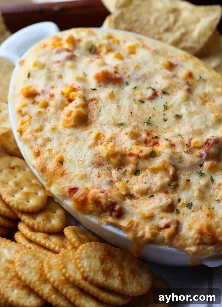 Warm and creamy hot corn dip is the ultimate party appetizer! It's baked until bubbly and delicious with chips, crackers, or veggies. Hot corn dip in an oval baking dish served next to assorted crackers.