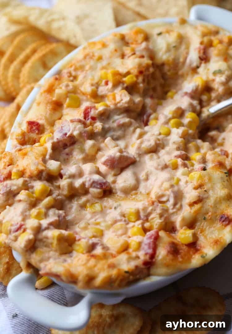 Warm and creamy hot corn dip is the ultimate party appetizer! It's baked until bubbly and delicious with chips, crackers, or veggies. Hot corn dip in an oval baking dish served next to assorted crackers.