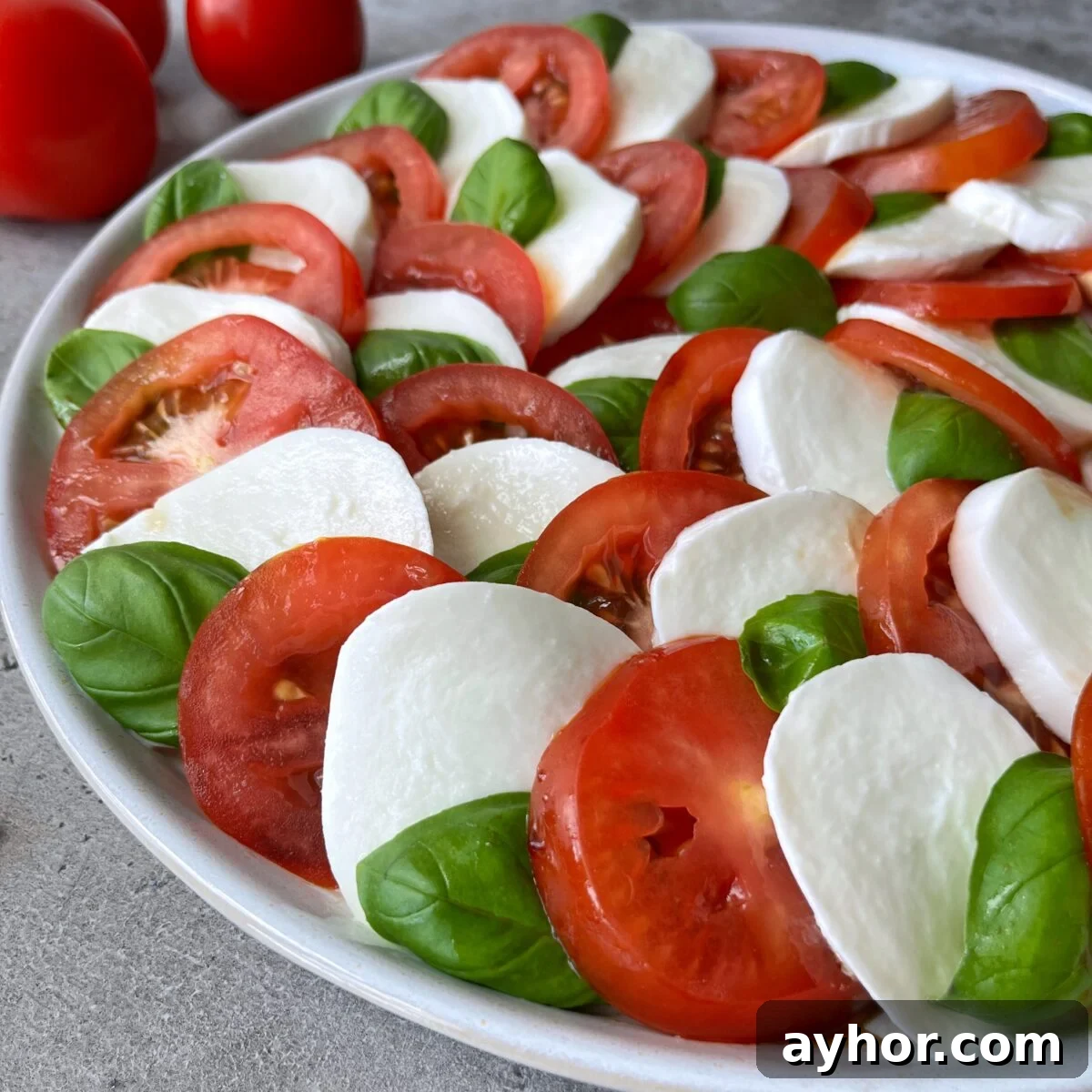Classic Tomato Caprese Salad with Fresh Basil and Mozzarella 3 A side view of a Tomato Caprese Salad featuring alternating slices of tomato, mozzarella cheese, and fresh basil leaves arranged in a beautiful circular pattern.