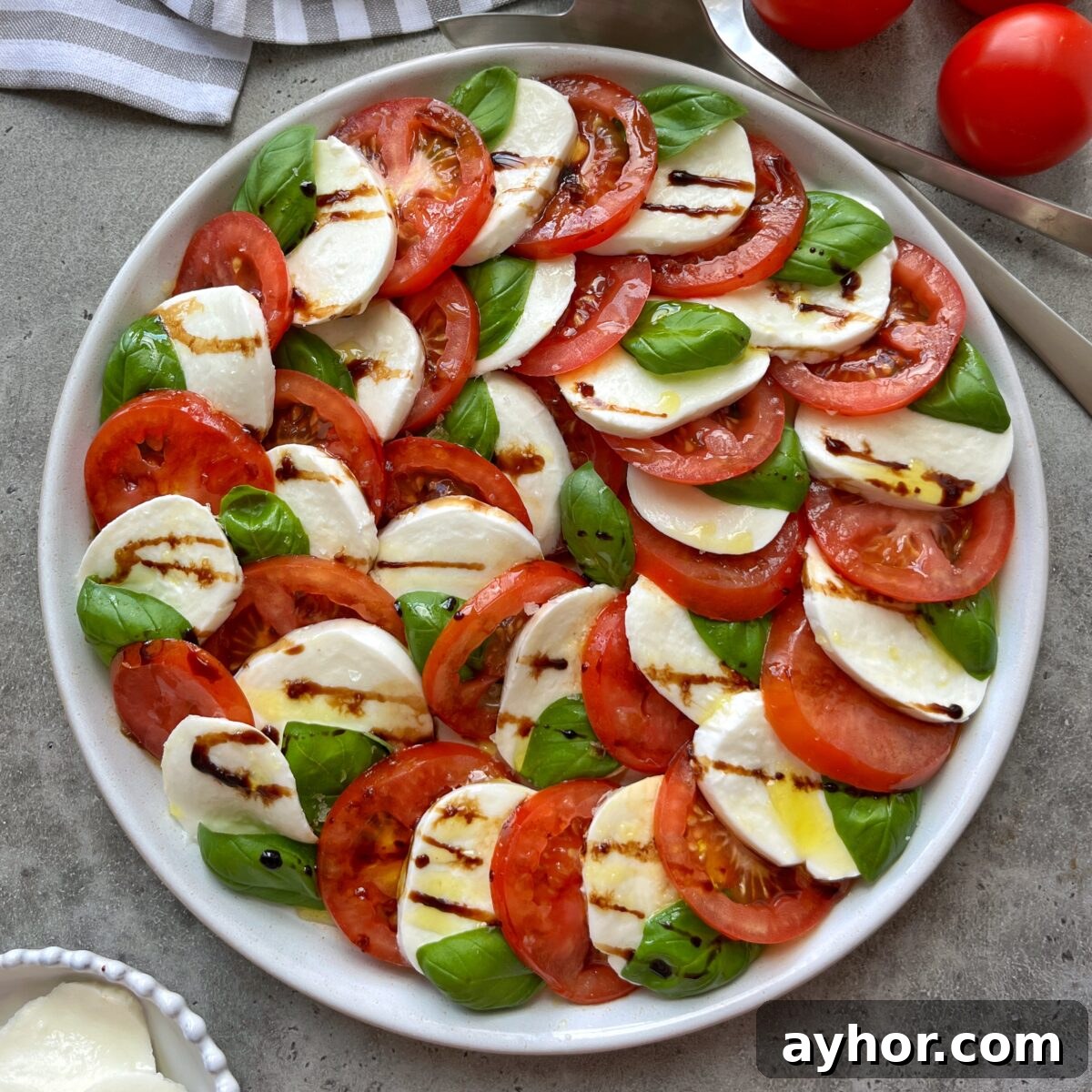 Classic Tomato Caprese Salad with Fresh Basil and Mozzarella 4 A Tomato Caprese Salad features sliced tomatoes, fresh mozzarella, basil leaves, and a drizzle of balsamic glaze, all artfully arranged in a circular pattern.