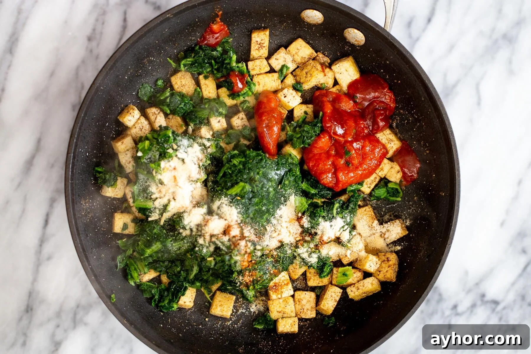 tofu cubes in a frying pan with red bell pepper and spinach 