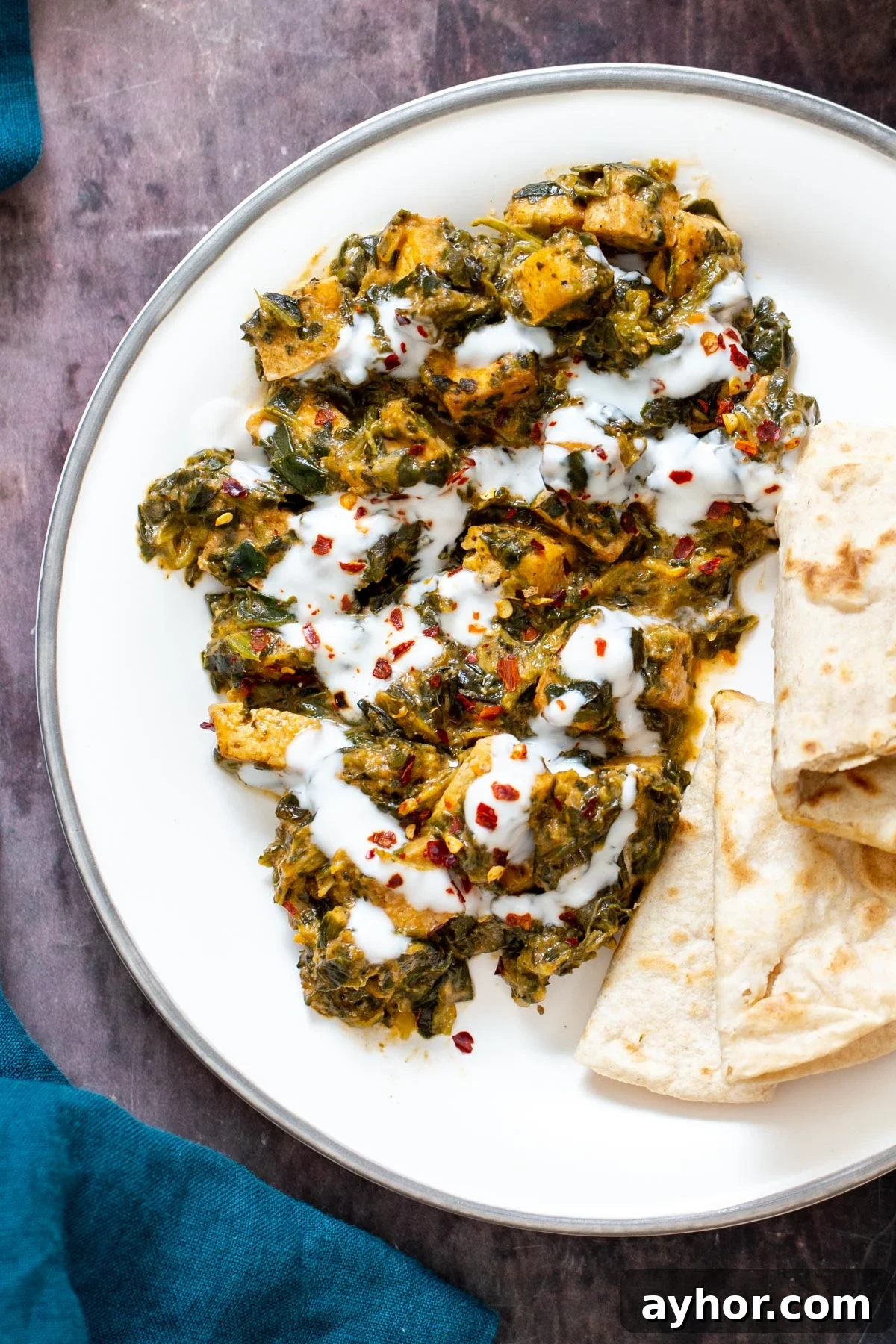 a serving of spinach tofu curry drizzled with yogurt and served with flatbread 