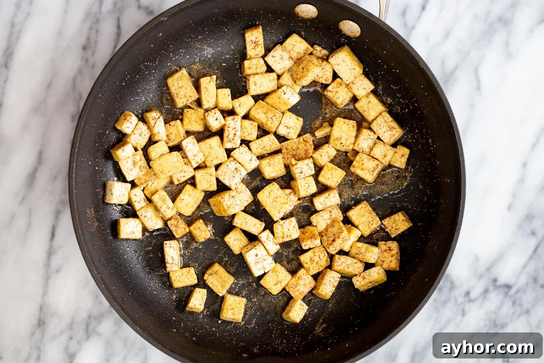 tofu cubes frying in a black skillet 
