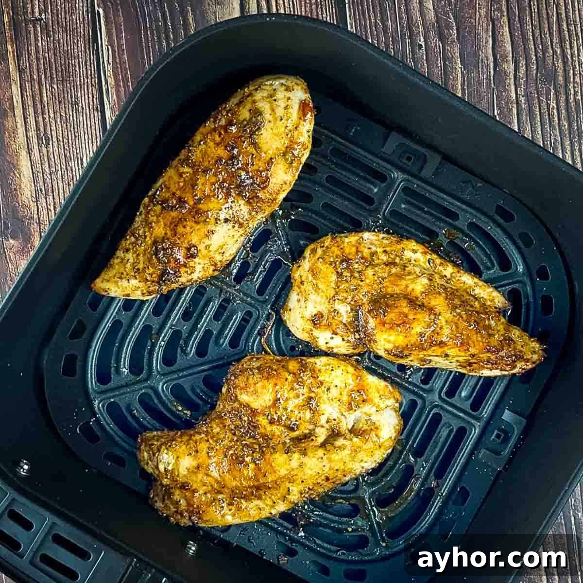 Three air fried thin chicken breasts resting in the air fryer basket.