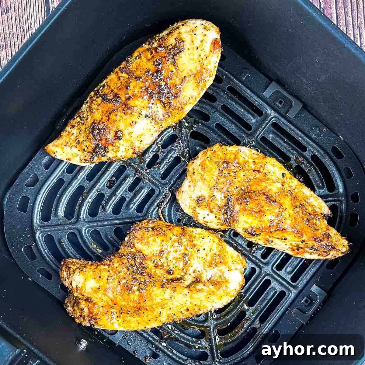 Seasoned and fully cooked thin chicken breasts in the air fryer basket.