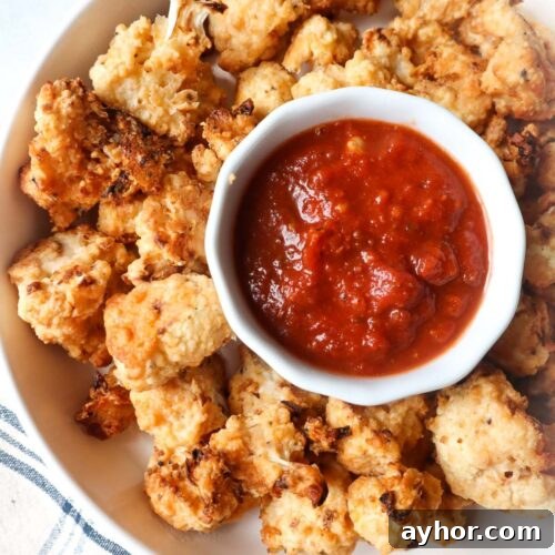 white bowl with air fryer cauliflower parmesan with warmed marinara in a cup