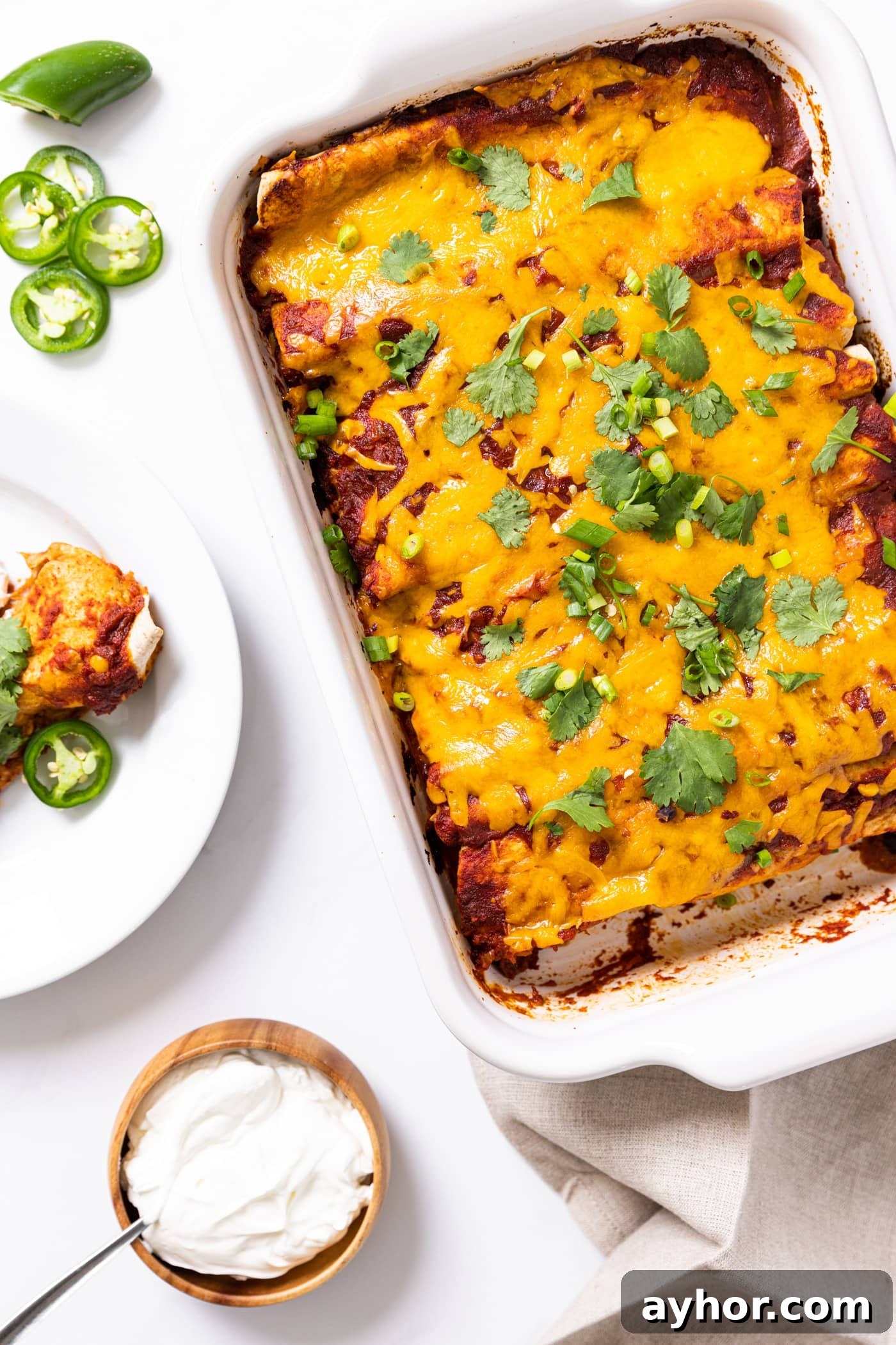 Creamy Chicken Enchiladas with Melted Cheese and Green Sauce 3 Top down view of white baking dish filled with chicken enchiladas topped with cilantro and plate filled with one slice of enchilada