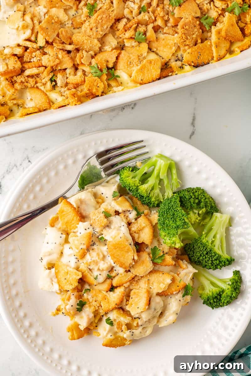 Overhead view of poppy seed chicken casserole on white plate with freshly steam broccoli.