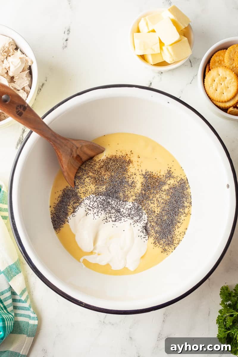 Ingredients for creamy sauce for poppy seed chicken in bowl with wooden spoon.