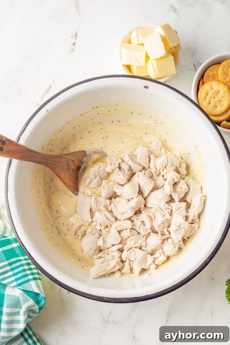 Chicken is added to the creamy sauce in bowl with wooden spoon.