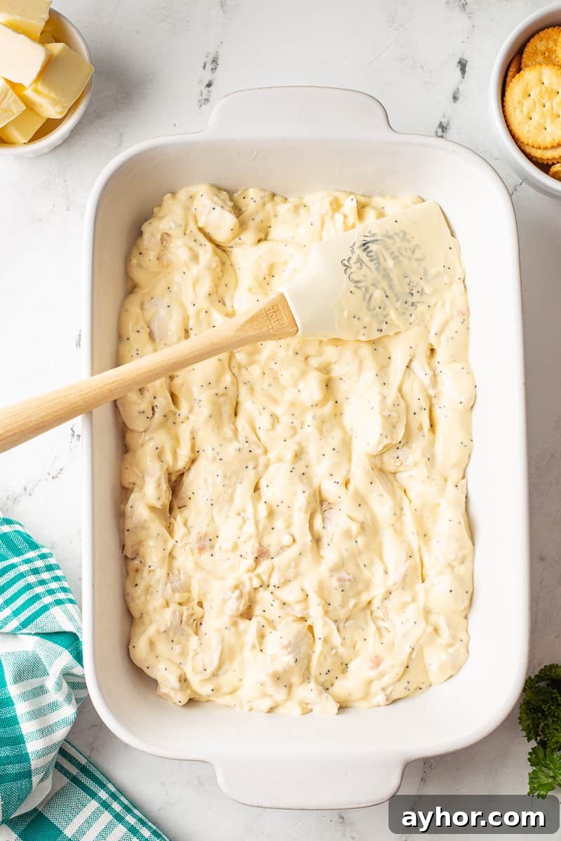 Chicken and cream sauce is spread out in casserole dish.
