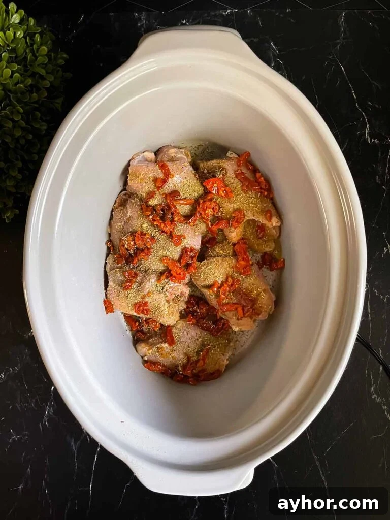 Raw chicken and sun-dried tomatoes in a slow cooker for Tuscan chicken.