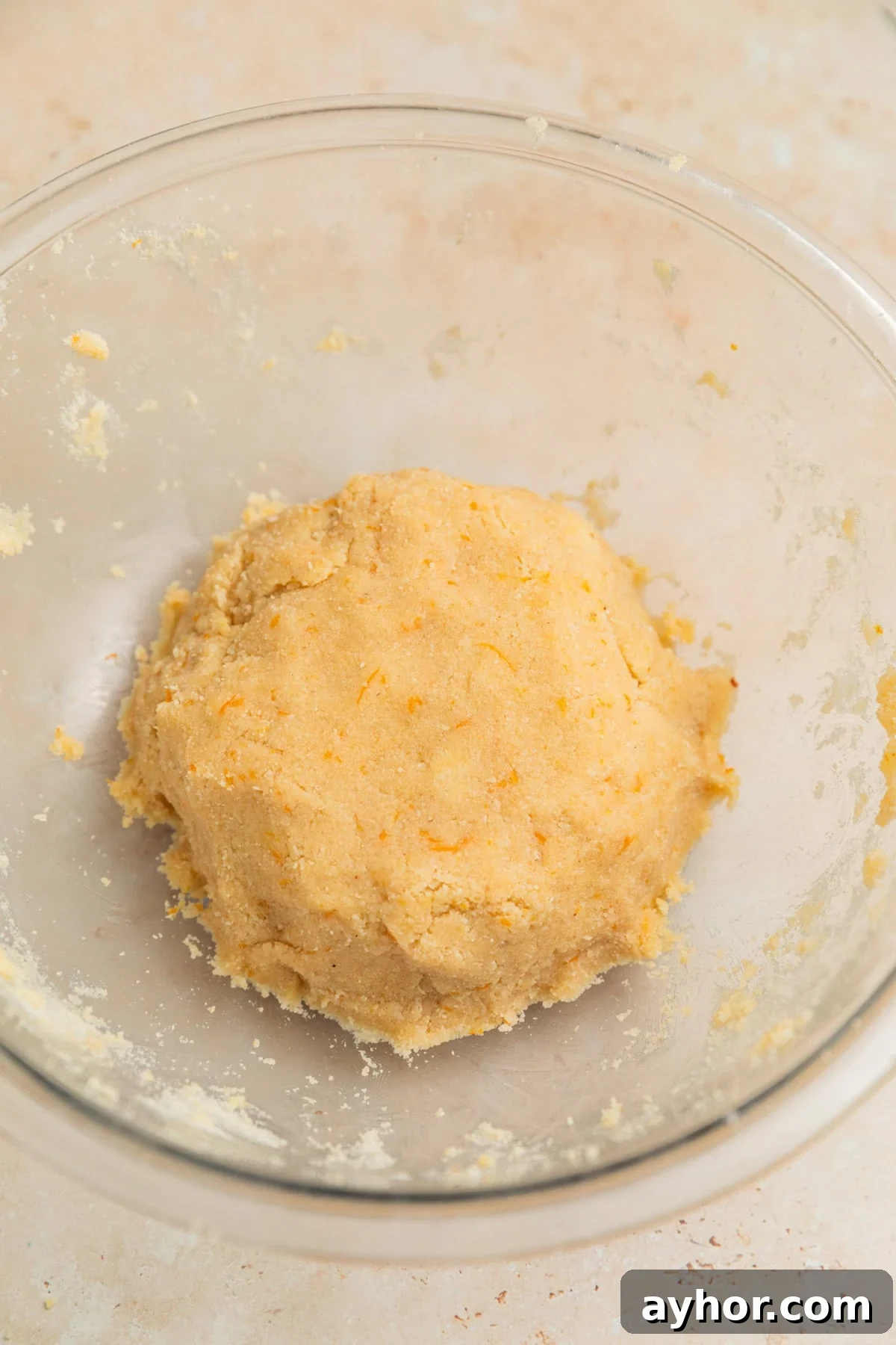 Ball of orange almond flour cookie dough in glass mixing bowl.