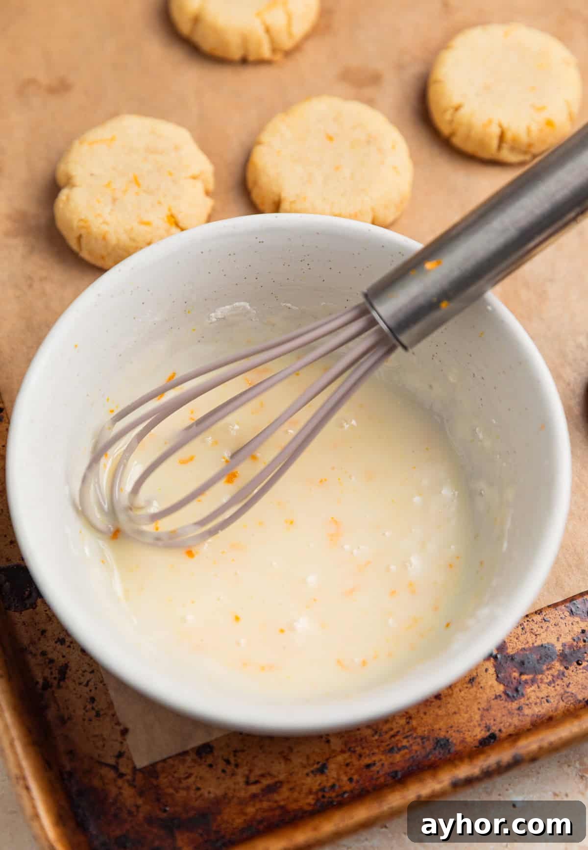 Orange icing in bowl with whisk.